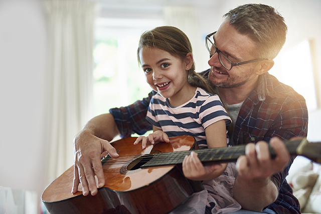 Shot of a little girl playing the guitar with her father