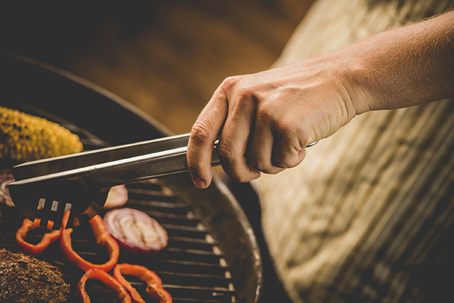 Still of a hand with barbecue tongs moving food on the barbecue