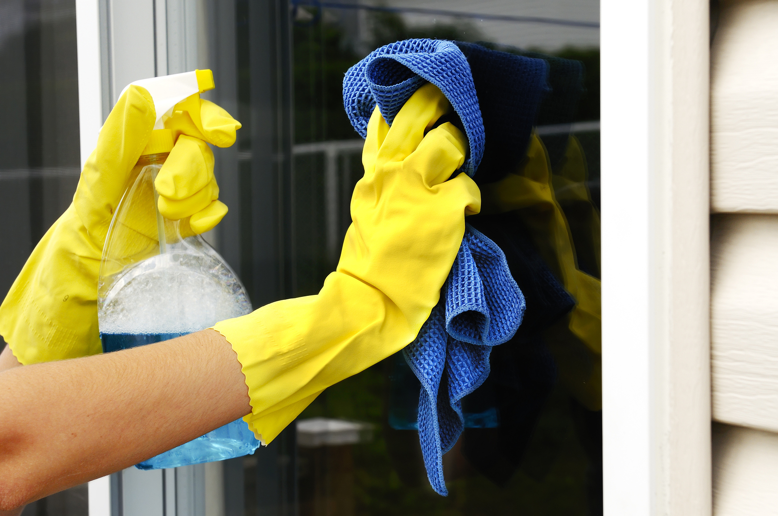 woman polishing glass door using microfiber cloth and yellow latex gloves