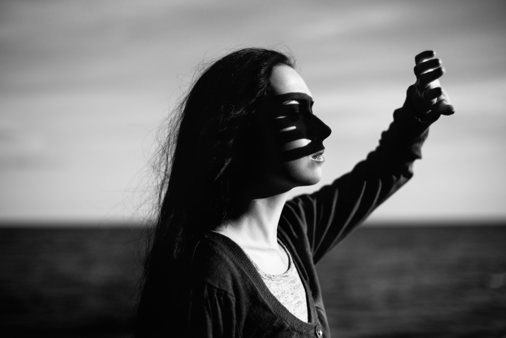 Real young girl in casual wear illuminated by the setting sun near the sea with her hand covering her face from sun light. black and white
