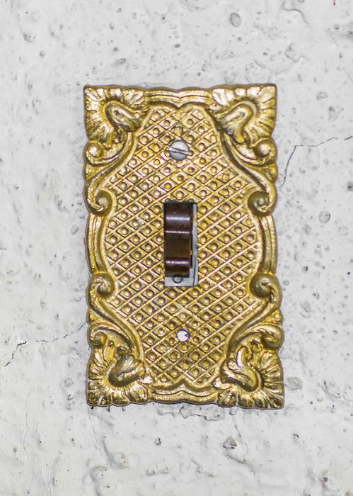 Old style ornate in golden tones lightswitch in white wall