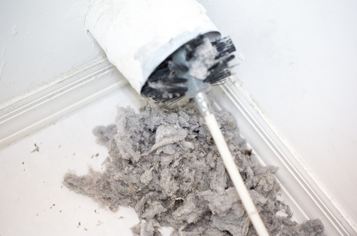 Dryer vent in a home being cleaned out with a round brush. There is a large pile of lint that has been removed from the vent on a white tiled floor. The walls and baseboards are white. The lint is gray. Taken with a Canon 5D Mark 3 camera. rm