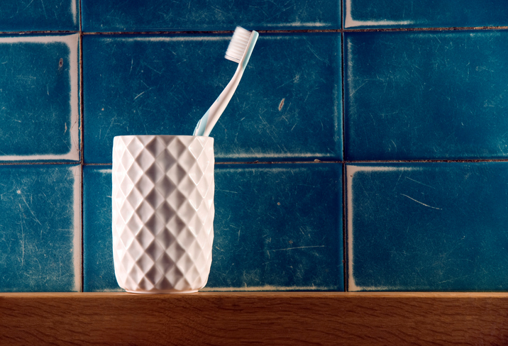 Single toothbrush in white beveled cup against blue tile
