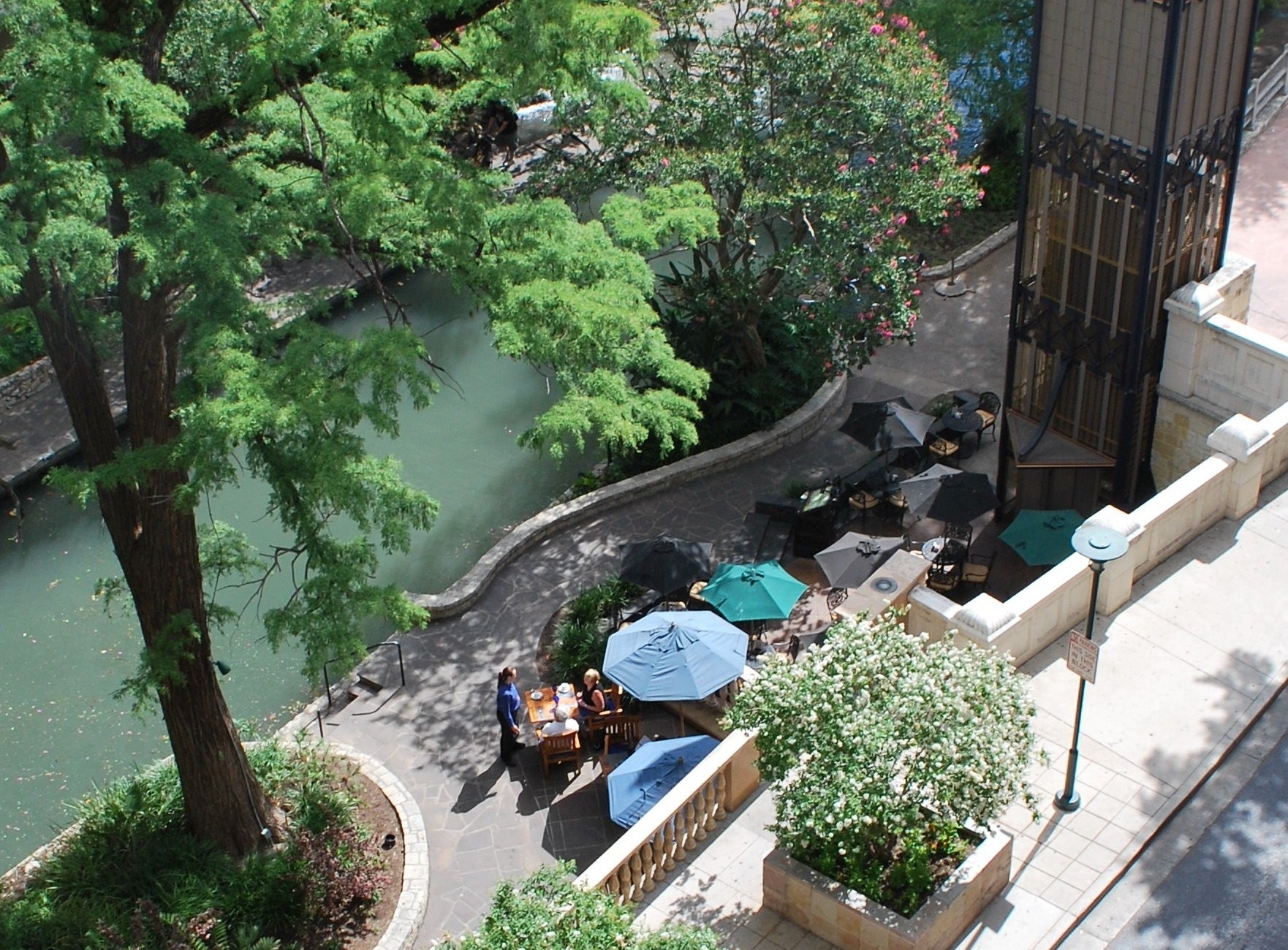 Scenic vacation spot for locals and visitors in historic San Antonio Texas. Man and woman have lunch outside by peaceful small river under colorful umbrellas. These patrons enjoy a quite meal and quaint view in the sunny afternoon.