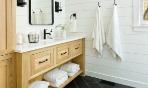 A remodeled bathroom with white tiles, a wooden vanity and white towels on wall hooks.